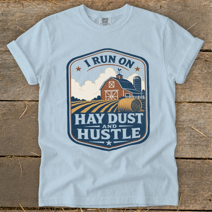 Light blue t-shirt with a farm scene and text "I RUN ON HAY DUST AND HUSTLE."