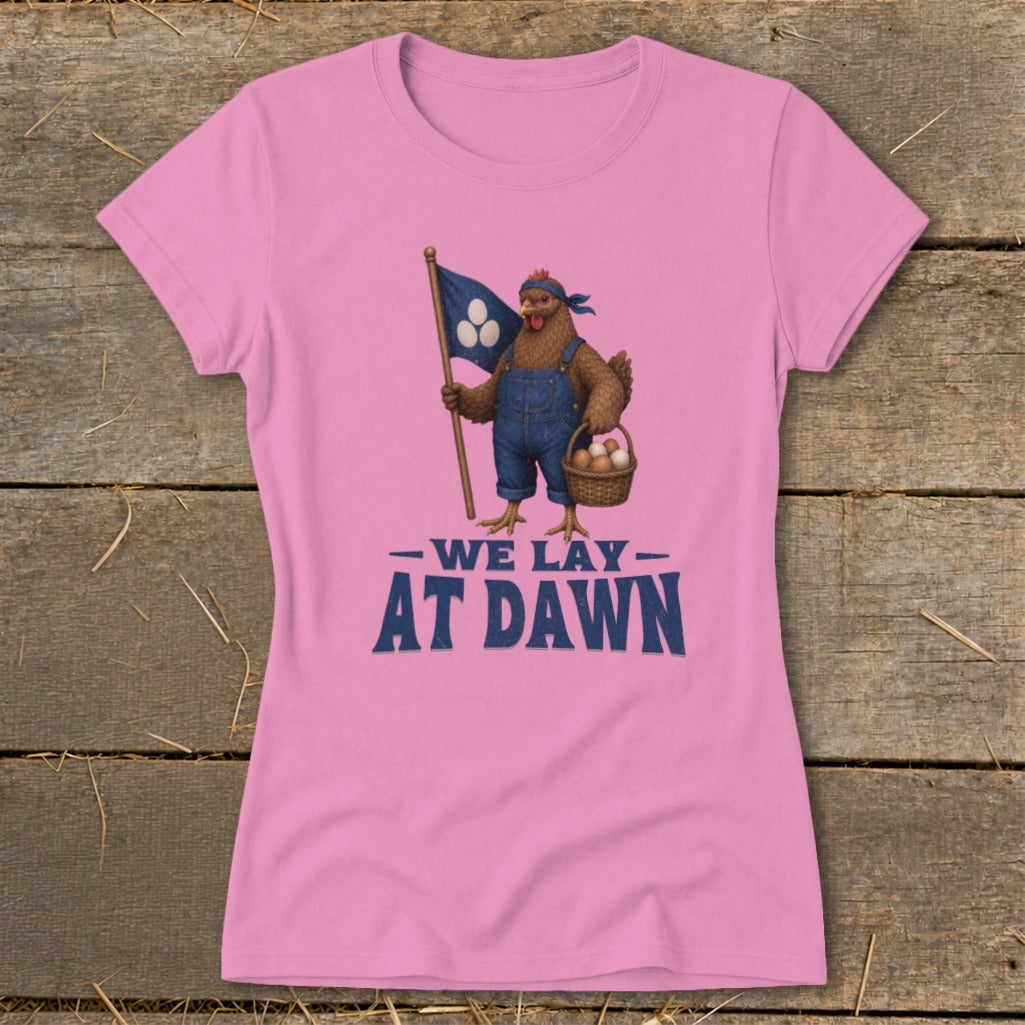 Pink t-shirt with a chicken in overalls holding a flag and basket of eggs, text "We lay at dawn."
