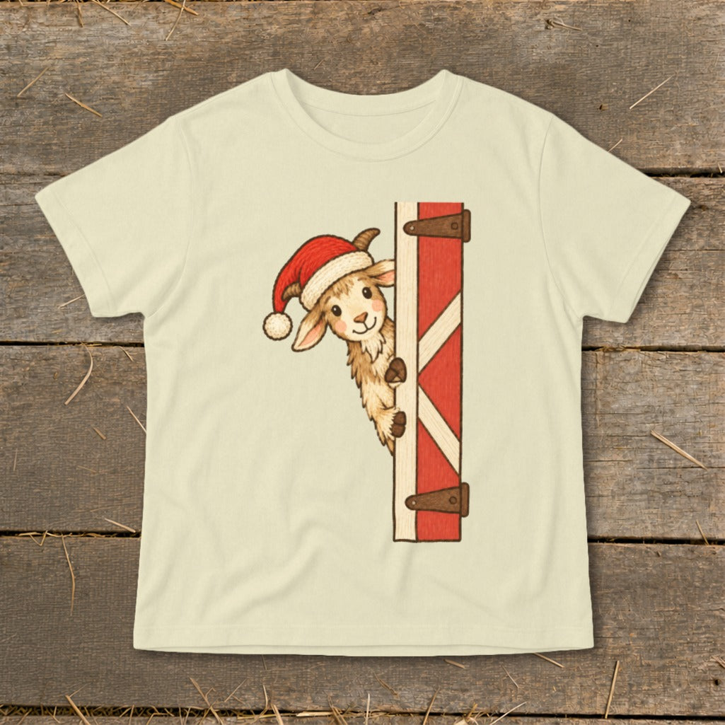 Cream t-shirt with a cartoon goat wearing a Santa hat peeking from behind a red barn door.