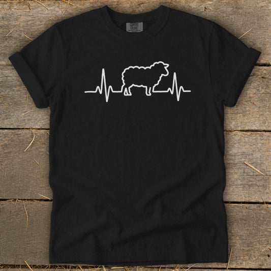 A black crewneck t-shirt featuring a white graphic of a sheep silhouetted against a heartbeat line, displayed flat on a wooden surface.