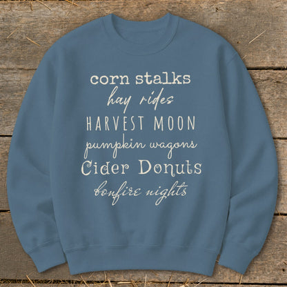 Blue sweatshirt with fall themes: corn stalks, hay rides, harvest moon, pumpkin wagons, cider donuts, bonfire nights.
