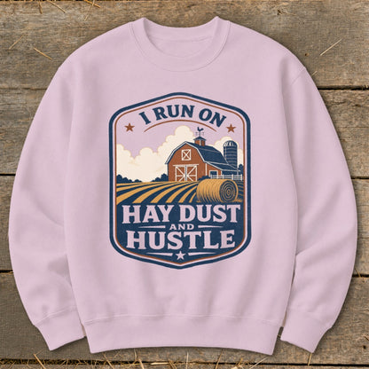 Light pink sweatshirt with a farm graphic that reads "I run on hay dust and hustle."