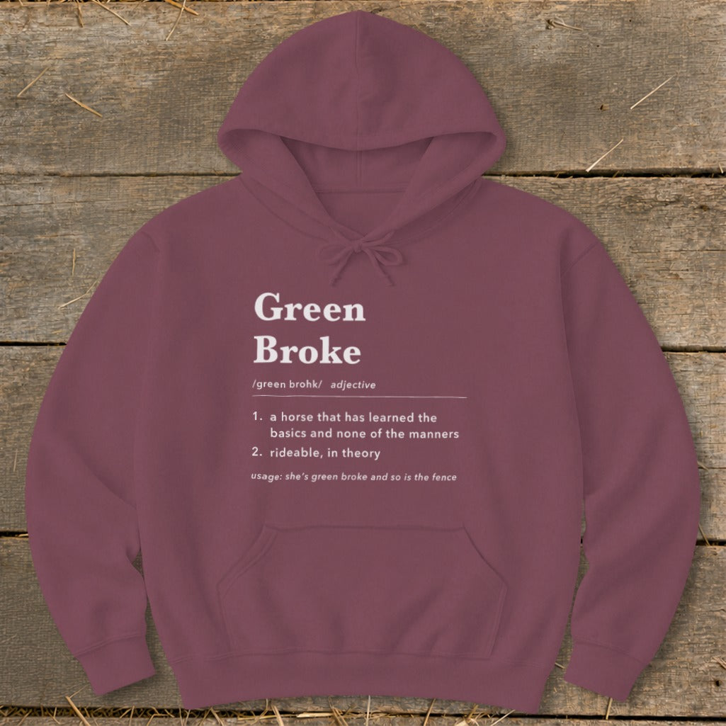 Maroon hoodie with white text defining Green Broke laid flat on rustic wood.