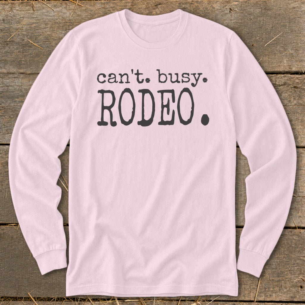 Pink long-sleeved t-shirt with "Can't. Busy. Rodeo." text graphic.