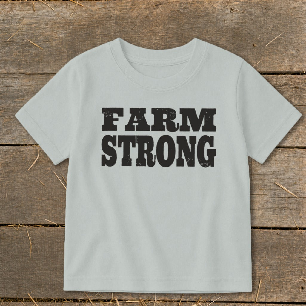 Light gray t-shirt featuring the black distressed text FARM STRONG laid flat on a rustic wooden surface.