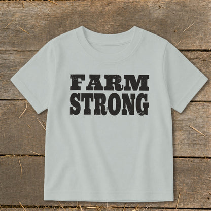 Light gray t-shirt featuring the black distressed text FARM STRONG laid flat on a rustic wooden surface.