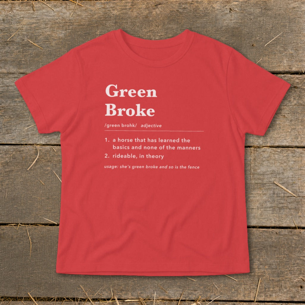 A red short-sleeved t-shirt with white text defining the phrase Green Broke laid on a wooden background.