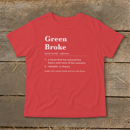 A red short-sleeved t-shirt with white text defining the phrase Green Broke laid on a wooden background.