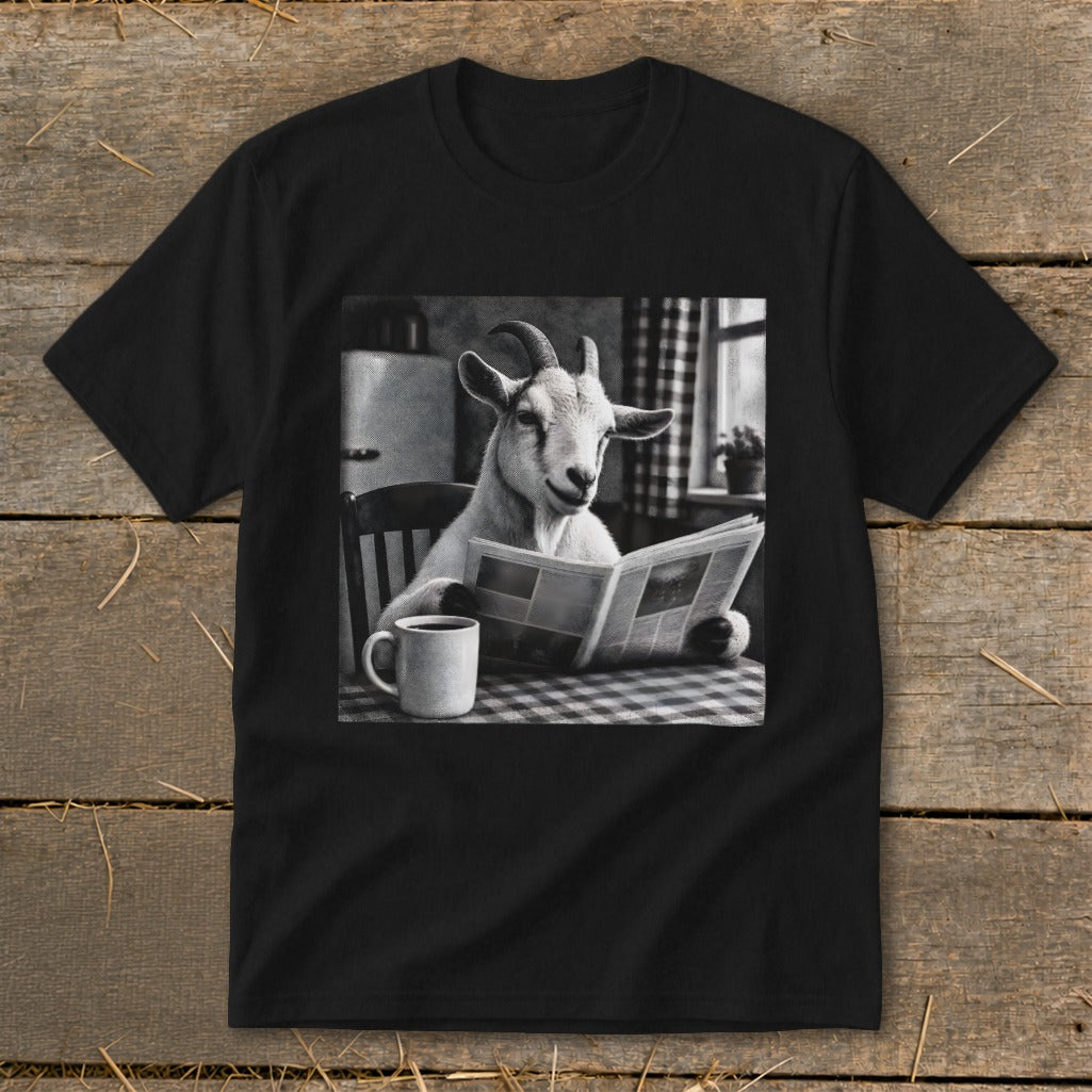 A black t-shirt features a graphic of a goat sitting at a kitchen table reading a newspaper beside a mug.