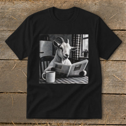 A black t-shirt features a graphic of a goat sitting at a kitchen table reading a newspaper beside a mug.