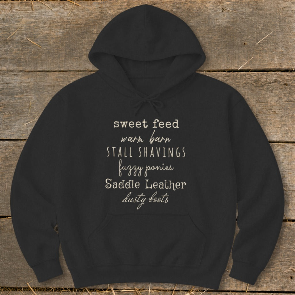 Black hoodie with text: sweet feed, warm barn, stall shavings, fuzzy ponies, saddle leather, dusty boots.