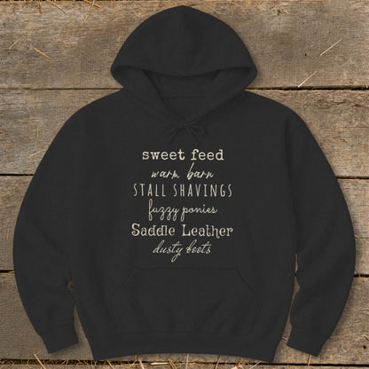 Black hoodie with text: sweet feed, warm barn, stall shavings, fuzzy ponies, saddle leather, dusty boots.