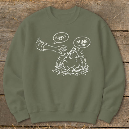 Green sweatshirt with a cartoon chicken protecting its eggs from a hand.