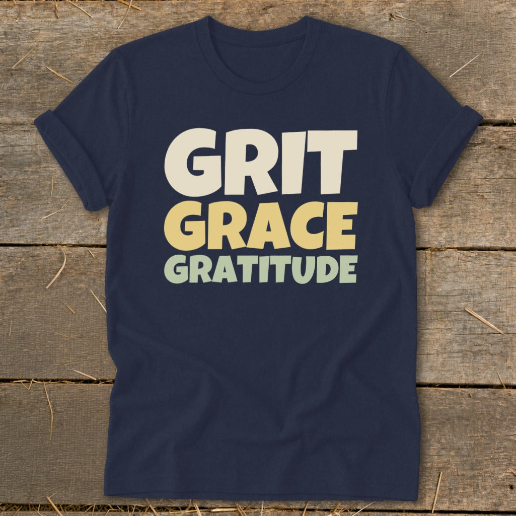 A navy blue t-shirt printed with the stacked text Grit, Grace, and Gratitude.