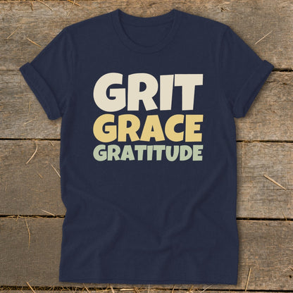 A navy blue t-shirt printed with the stacked text Grit, Grace, and Gratitude.