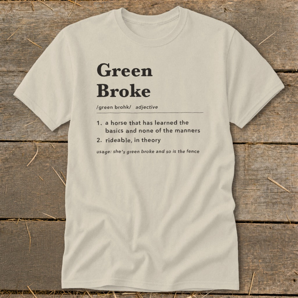 A light cream t-shirt with black text defining the equestrian term green broke on a wooden background.