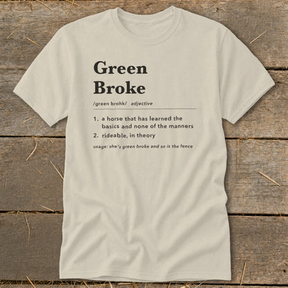 A light cream t-shirt with black text defining the equestrian term green broke on a wooden background.