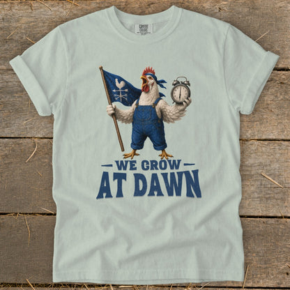 Chicken in overalls holding flag and alarm clock, "We Grow At Dawn" text.
