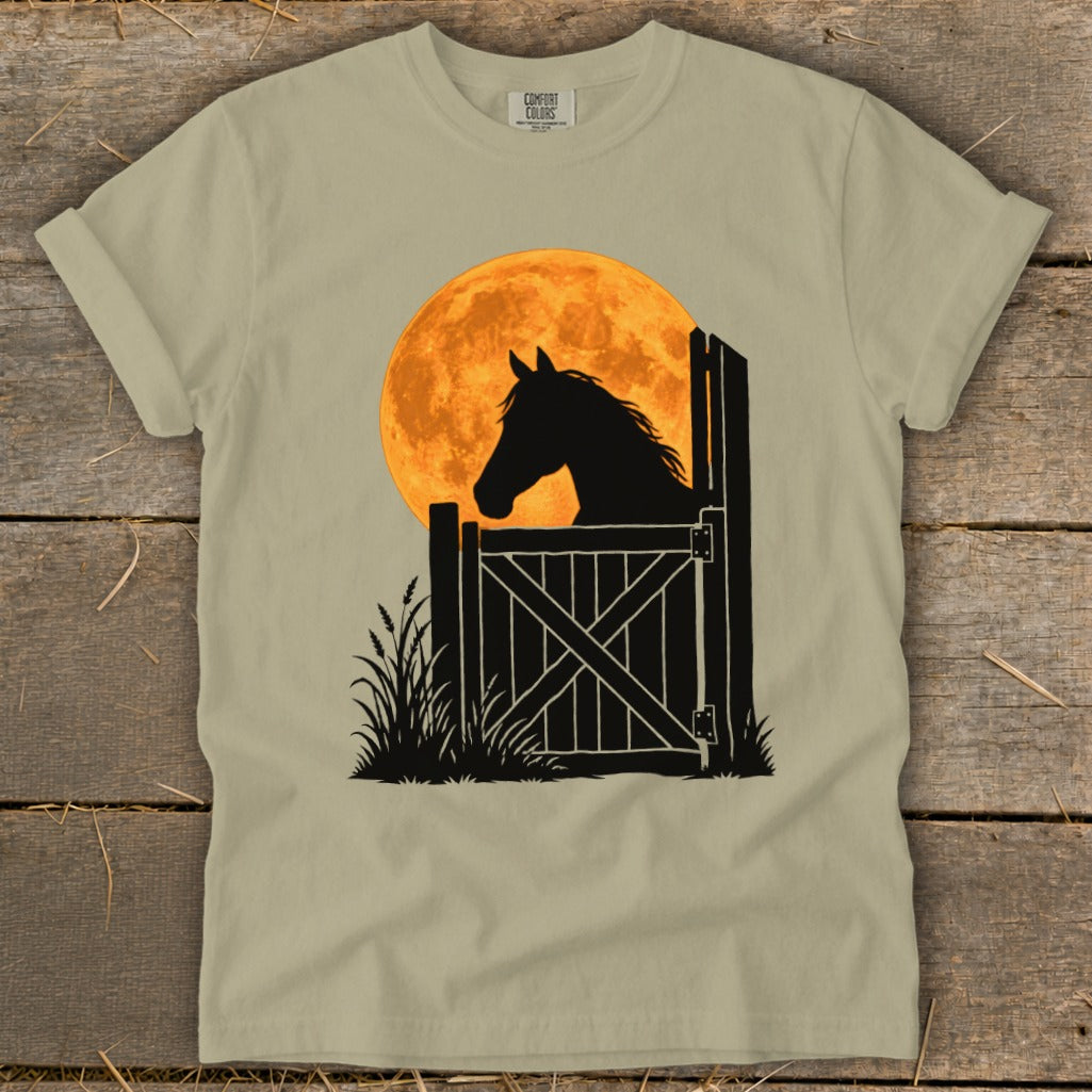 Sage green t-shirt featuring a black silhouette of a horse looking out a stable door against a large orange moon.