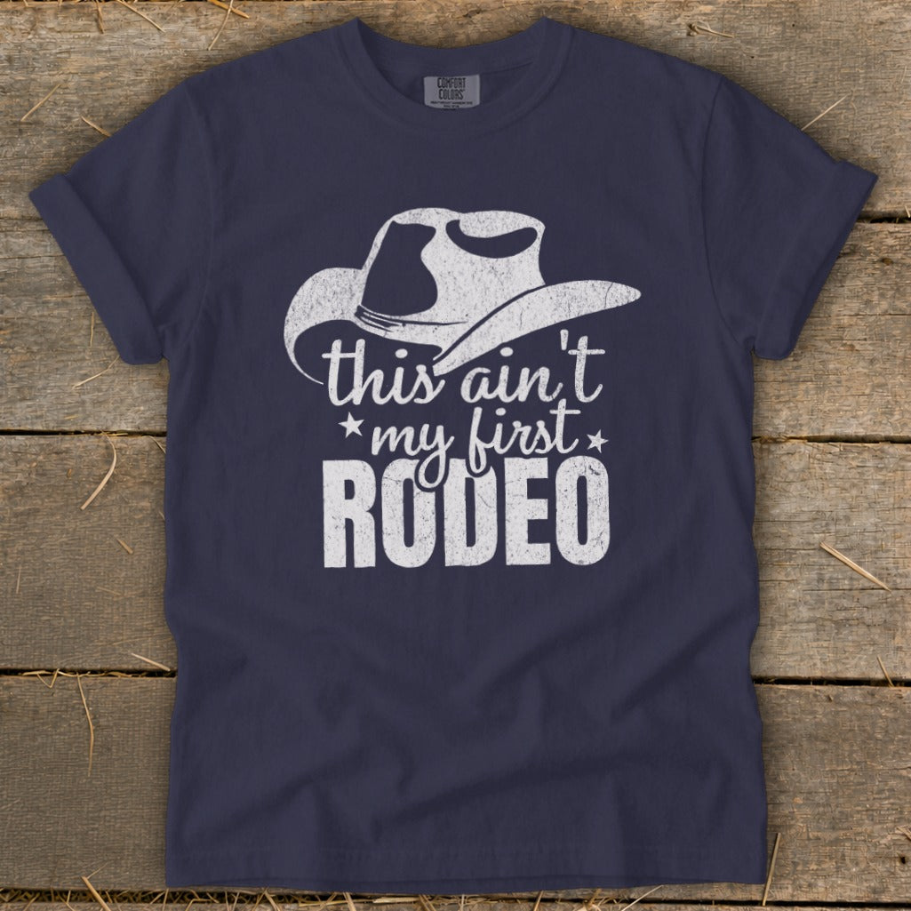 Navy t-shirt with white distressed cowboy hat graphic and "this ain't my first RODEO" text.