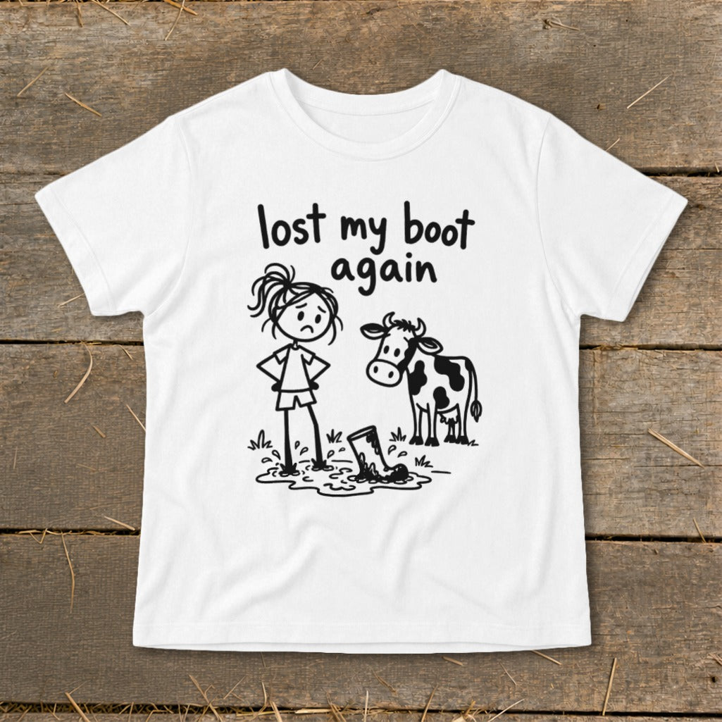 A white t-shirt featuring a stick-figure drawing of a girl and a cow standing near a muddy boot, with the text "lost my boot again."