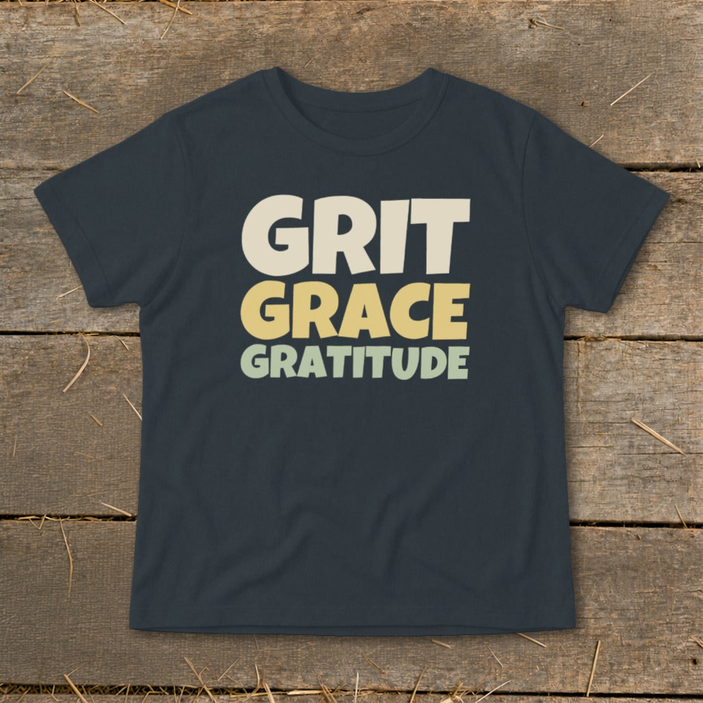 Dark grey t-shirt featuring the stacked text Grit, Grace, Gratitude on a wooden surface.