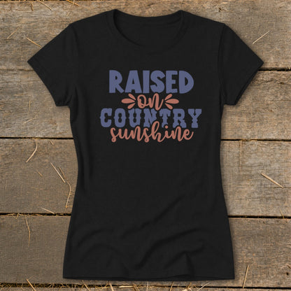 Black t-shirt with "Raised on country sunshine" text in blue and coral.