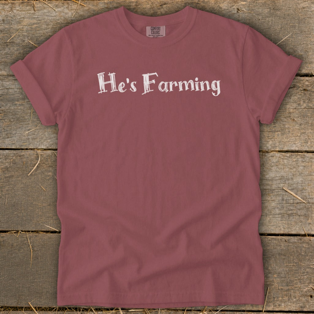 Rose-colored t-shirt with white text reading "He's Farming" and Comfort Colors tag.