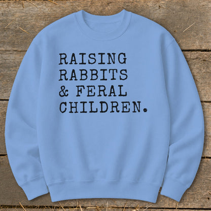 Light blue sweatshirt with black text reading "Raising Rabbits & Feral Children."