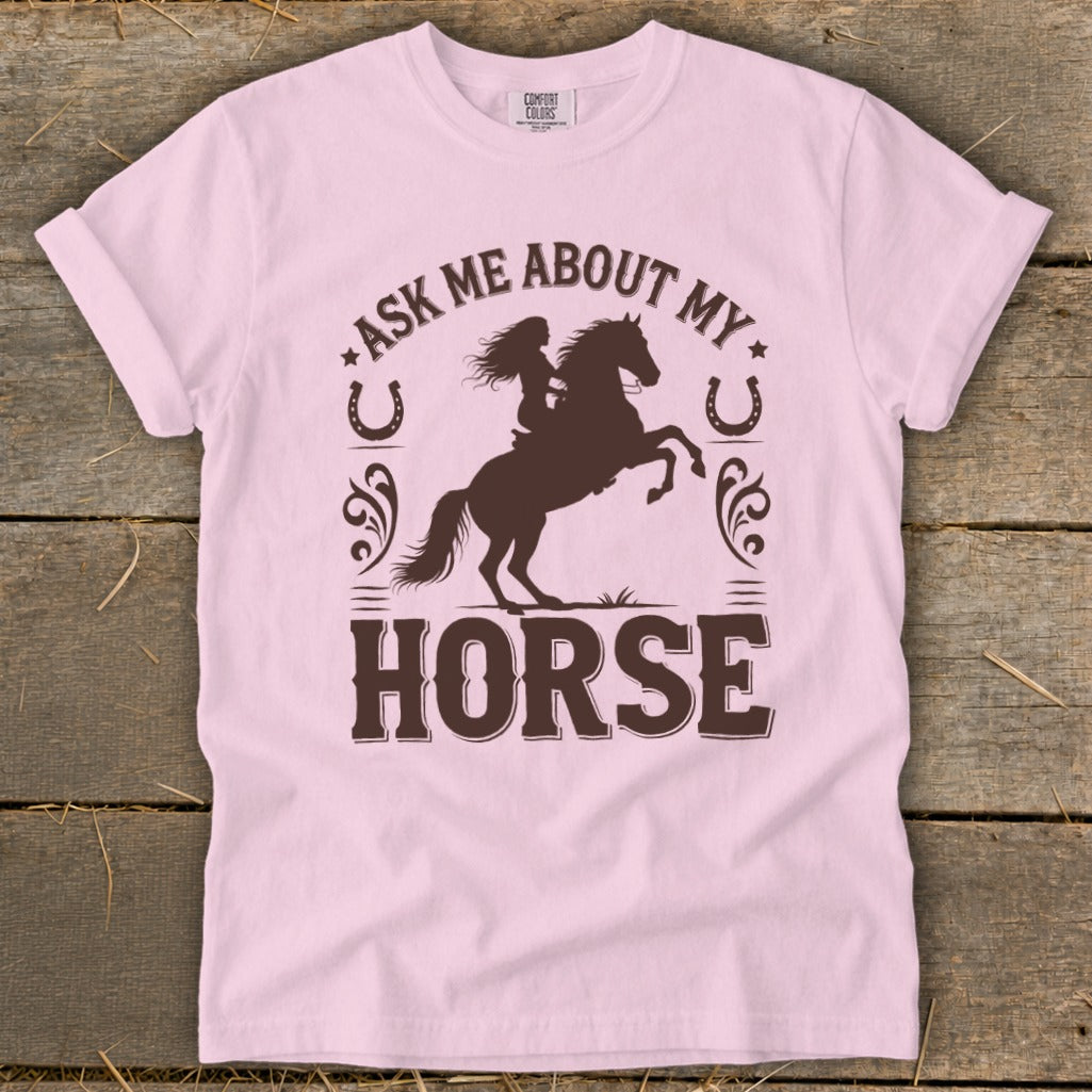 Light pink t-shirt with brown graphic of a girl riding a bucking horse and text.