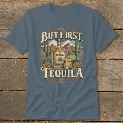 Blue t-shirt graphic with tequila bottle, shot glass, cacti, and desert landscape. Text reads "But First, Tequila."