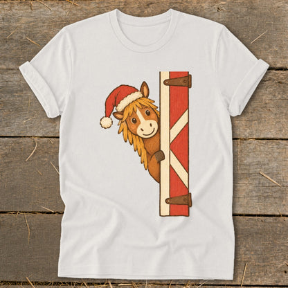 Horse wearing a Santa hat peeking from a red barn door.
