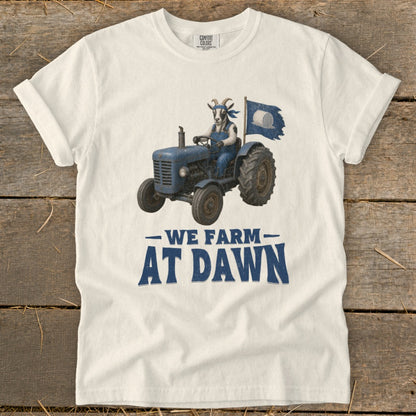 White t-shirt with a goat driving a blue tractor and the text "WE FARM AT DAWN."