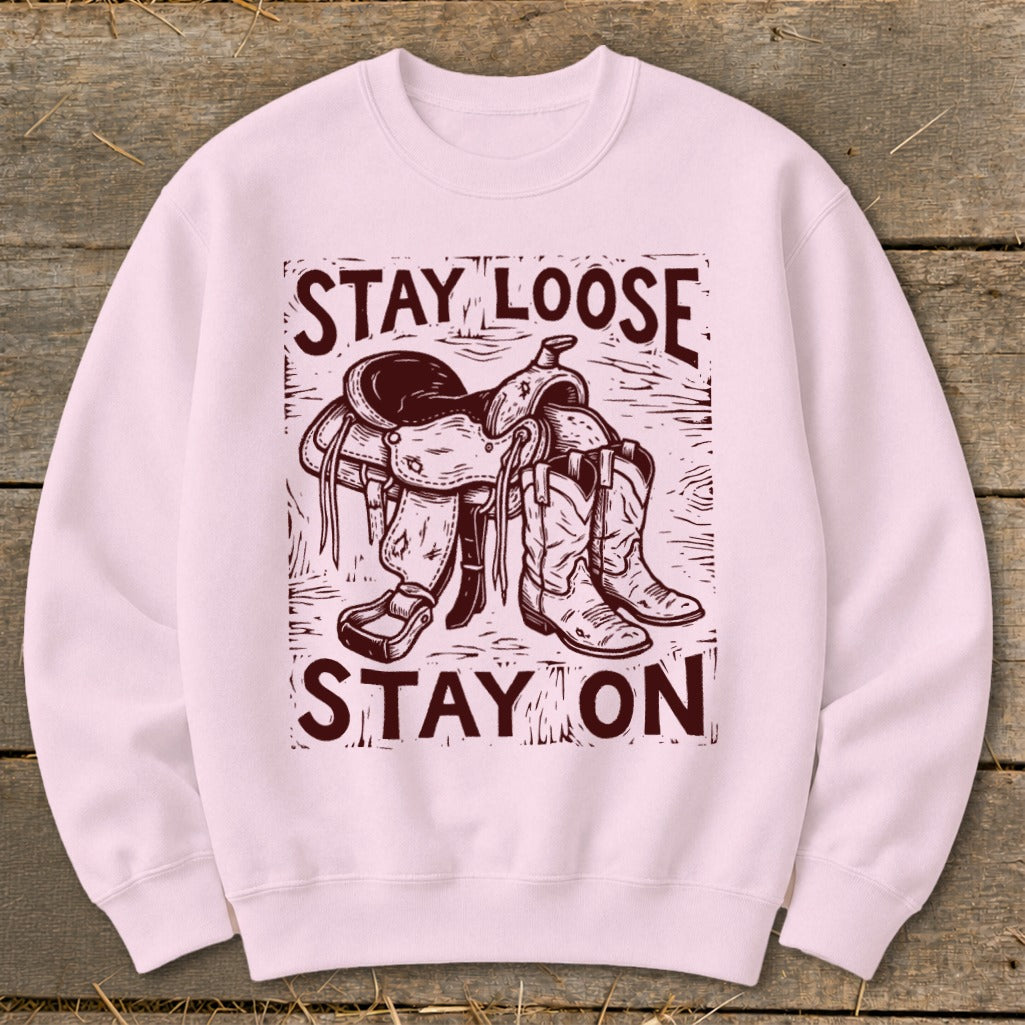 Pink sweatshirt with a woodcut-style graphic of a saddle and cowboy boots, reading "STAY LOOSE STAY ON".