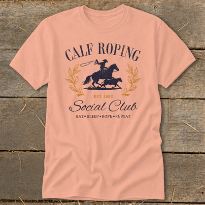 Calf Roping Social Club graphic on a peach t-shirt, with text and rodeo scene.
