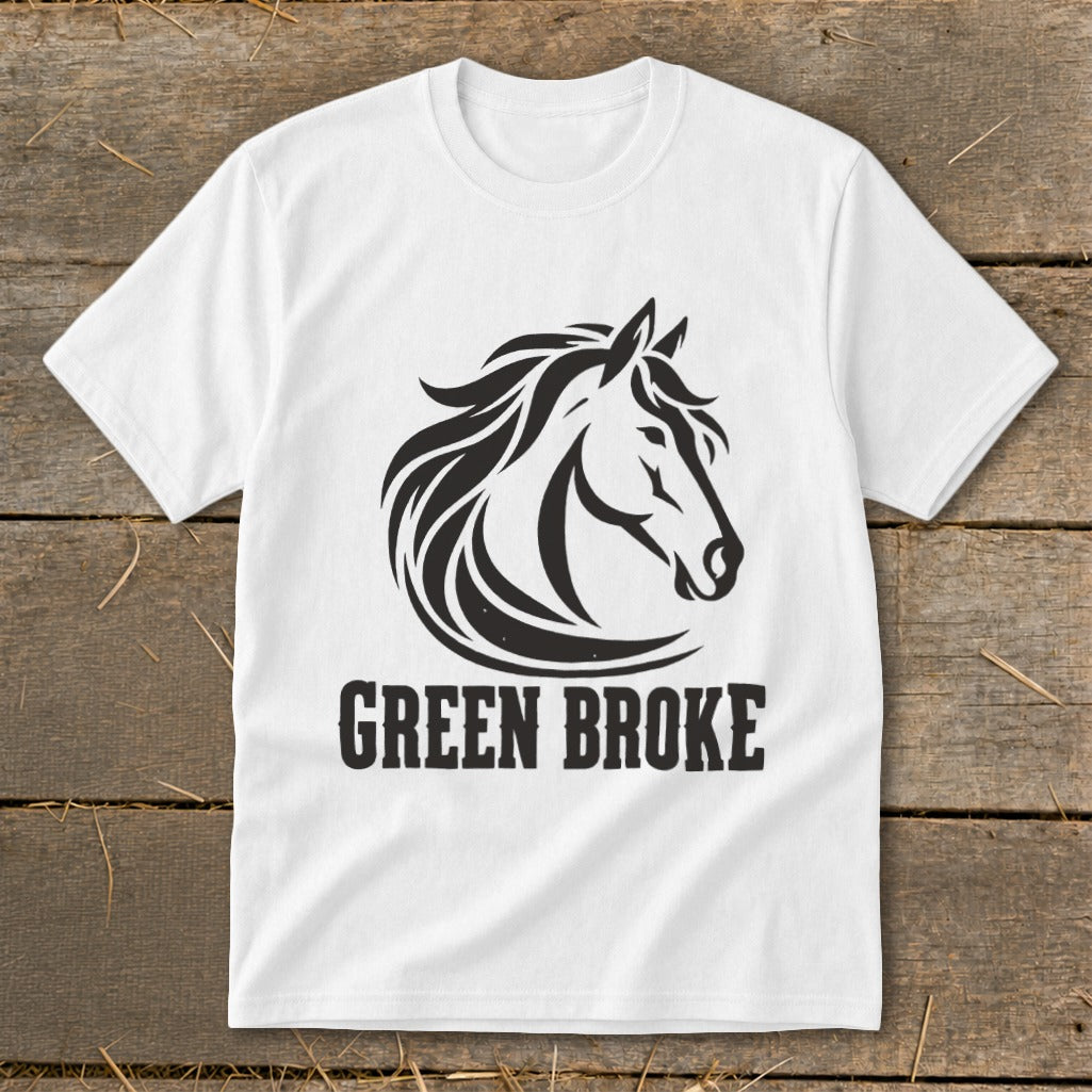 A white t-shirt laid flat on a wooden surface, featuring a black graphic of a horse head and the text "GREEN BROKE".