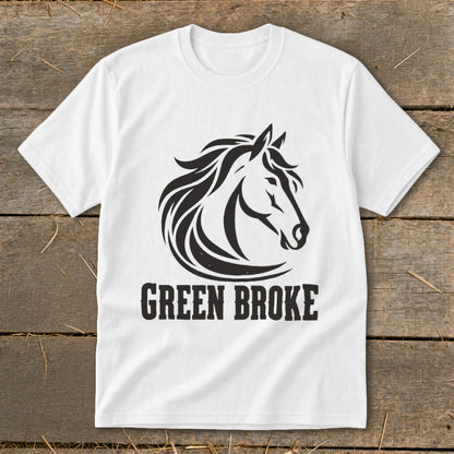 A white t-shirt laid flat on a wooden surface, featuring a black graphic of a horse head and the text "GREEN BROKE".