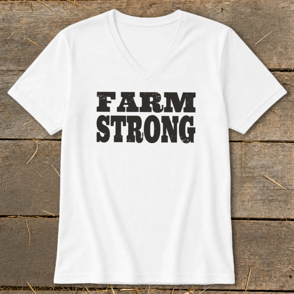 A white V-neck t-shirt with black distressed text reading FARM STRONG centered on the chest, laid flat on a weathered wooden surface.