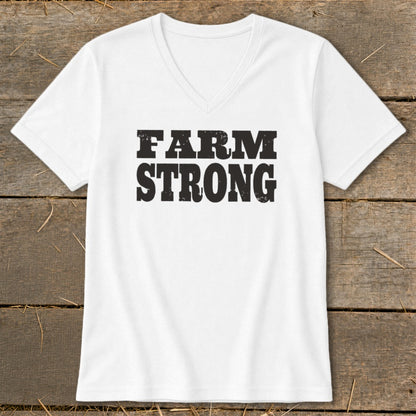 A white V-neck t-shirt with black distressed text reading FARM STRONG centered on the chest, laid flat on a weathered wooden surface.