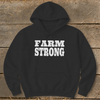 Black hooded sweatshirt with white distressed text reading FARM STRONG on a wooden surface.