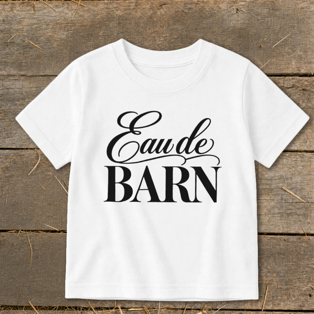 White t-shirt with black text "Eau de BARN" on rustic wood background.