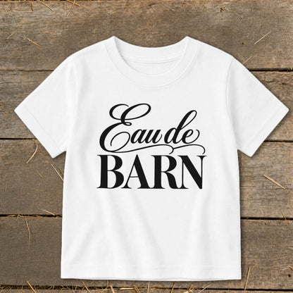 White t-shirt with black text "Eau de BARN" on rustic wood background.