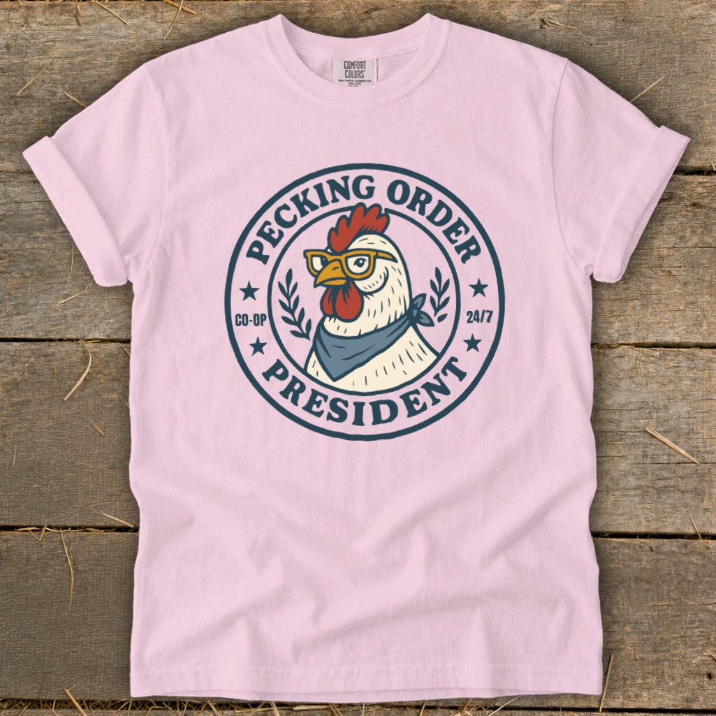 Pink t-shirt with a graphic of a chicken wearing glasses and a bandana, text reads "Pecking Order President".