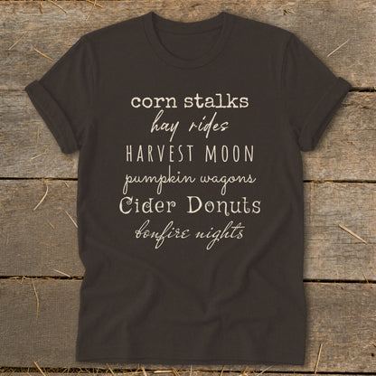 Dark t-shirt with "corn stalks, hay rides, harvest moon, pumpkin wagons, cider donuts, bonfire nights" text.