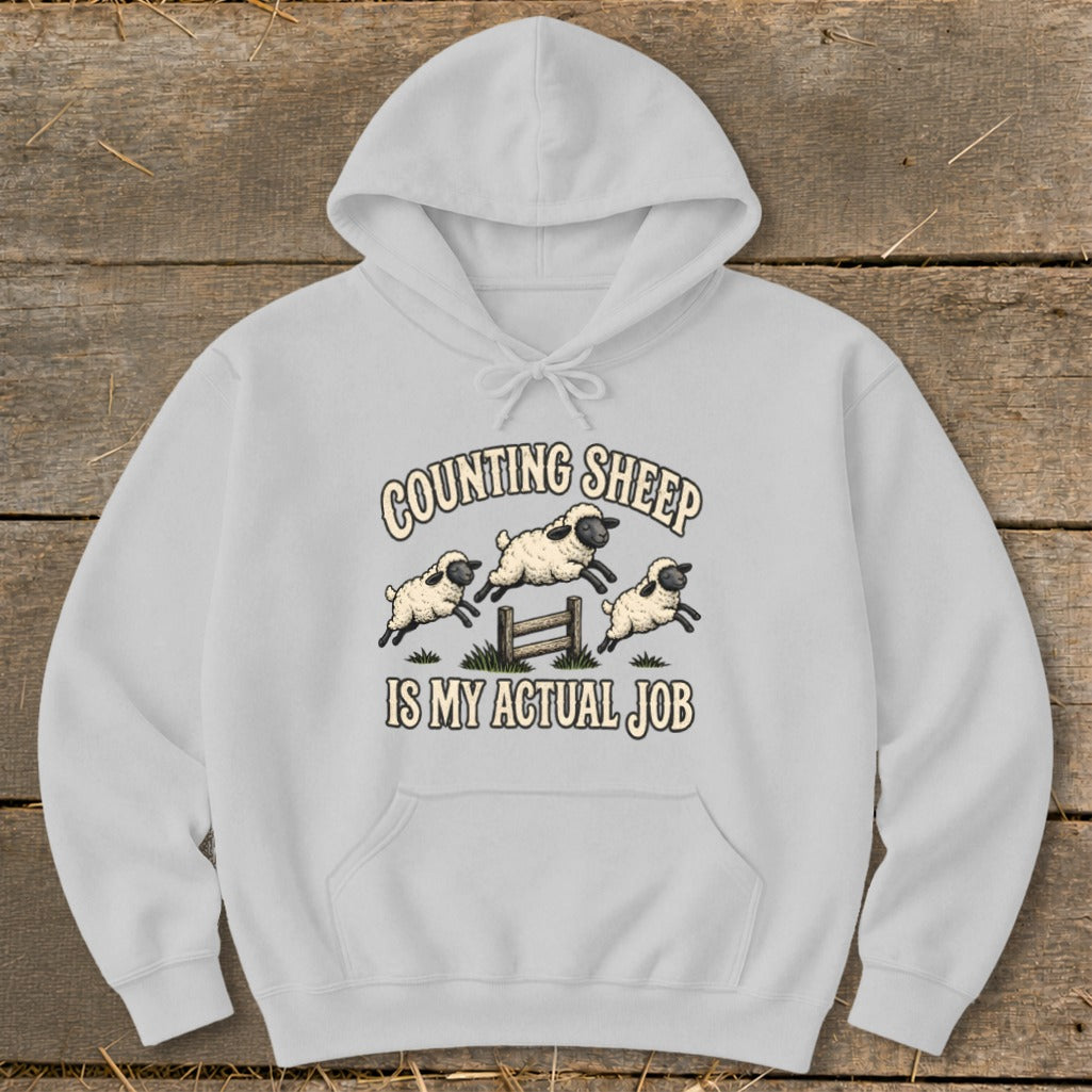 Light grey hoodie with "Counting Sheep Is My Actual Job" text and jumping sheep graphic.