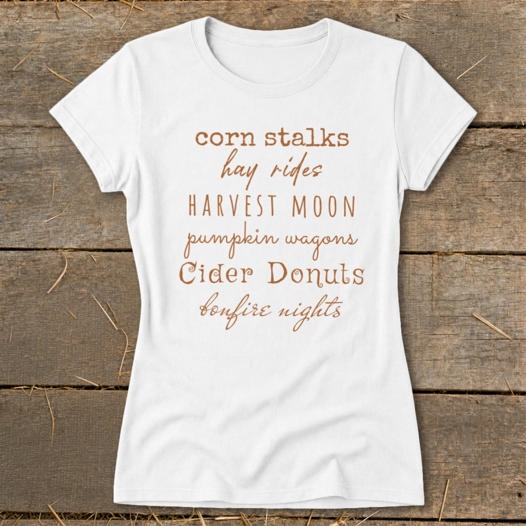 White t-shirt with "corn stalks, hay rides, harvest moon, pumpkin wagons, cider donuts, bonfire nights" text.
