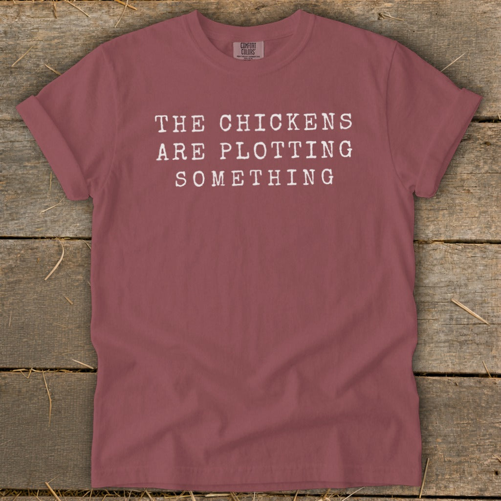 Maroon t-shirt with white text reading "THE CHICKENS ARE PLOTTING SOMETHING."