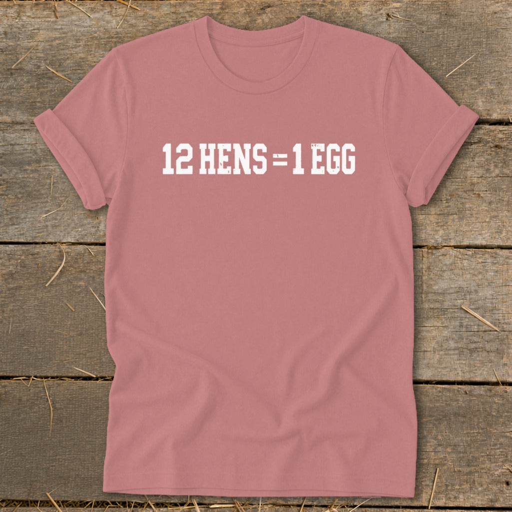 Dusty pink t-shirt featuring the white text 12 HENS = 1 EGG, laid flat on a wooden surface.