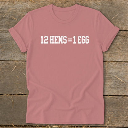 Dusty pink t-shirt featuring the white text 12 HENS = 1 EGG, laid flat on a wooden surface.