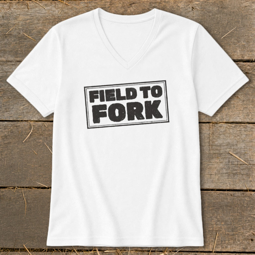 A white V-neck t-shirt rests on a rustic wooden background, featuring the words Field to Fork printed in black inside a box.